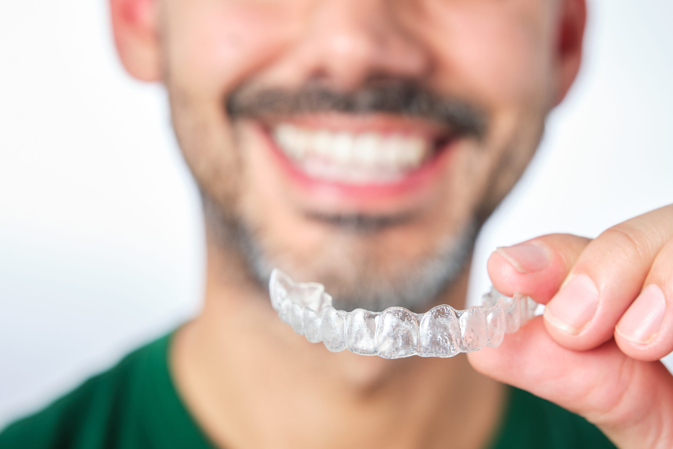 closeup man hand holding transparent retainer with unrecognizable bearded man face in unfocused background on white background