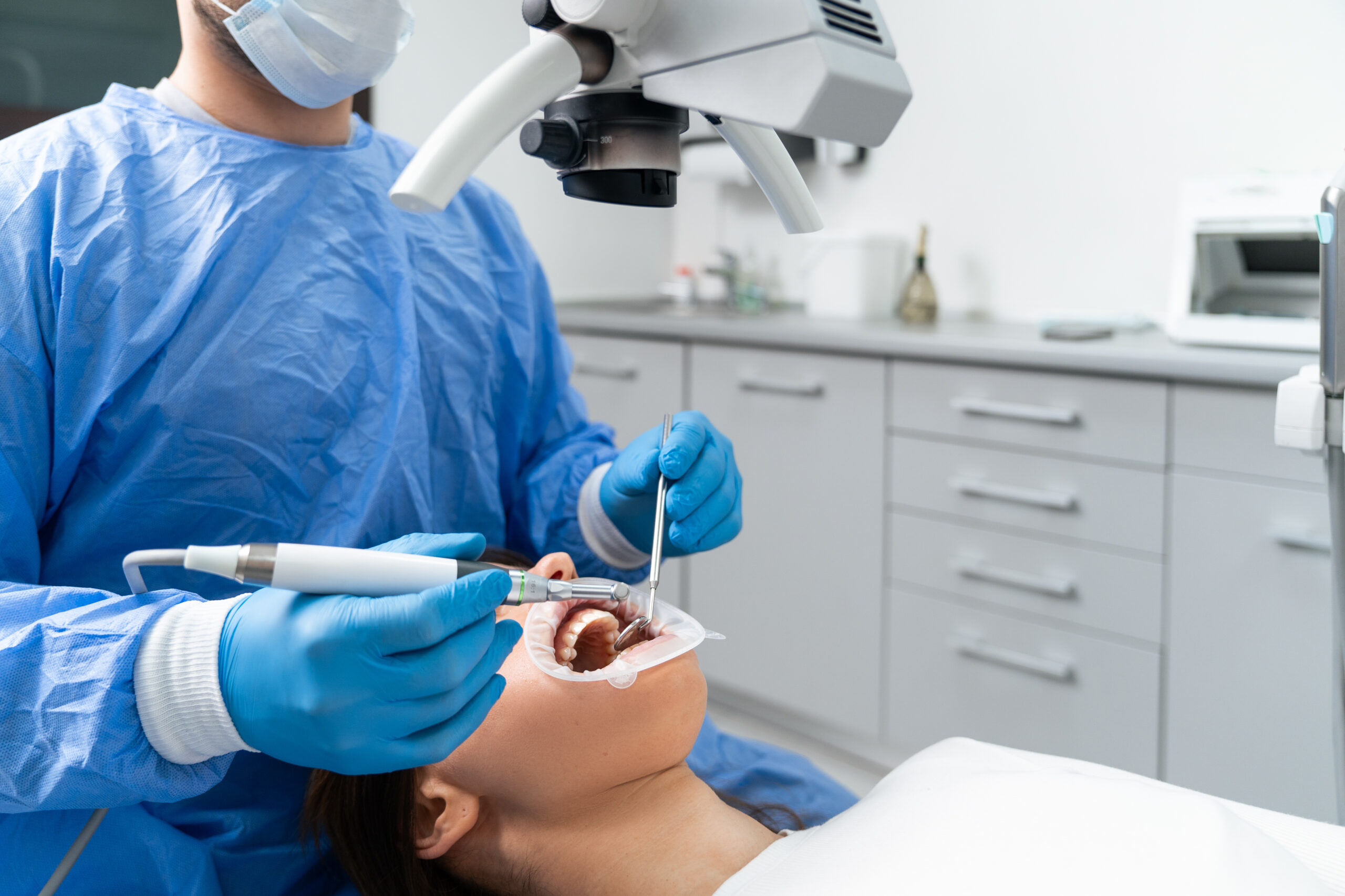 A young European male dentist treats a patient's teeth using a modern microscope.